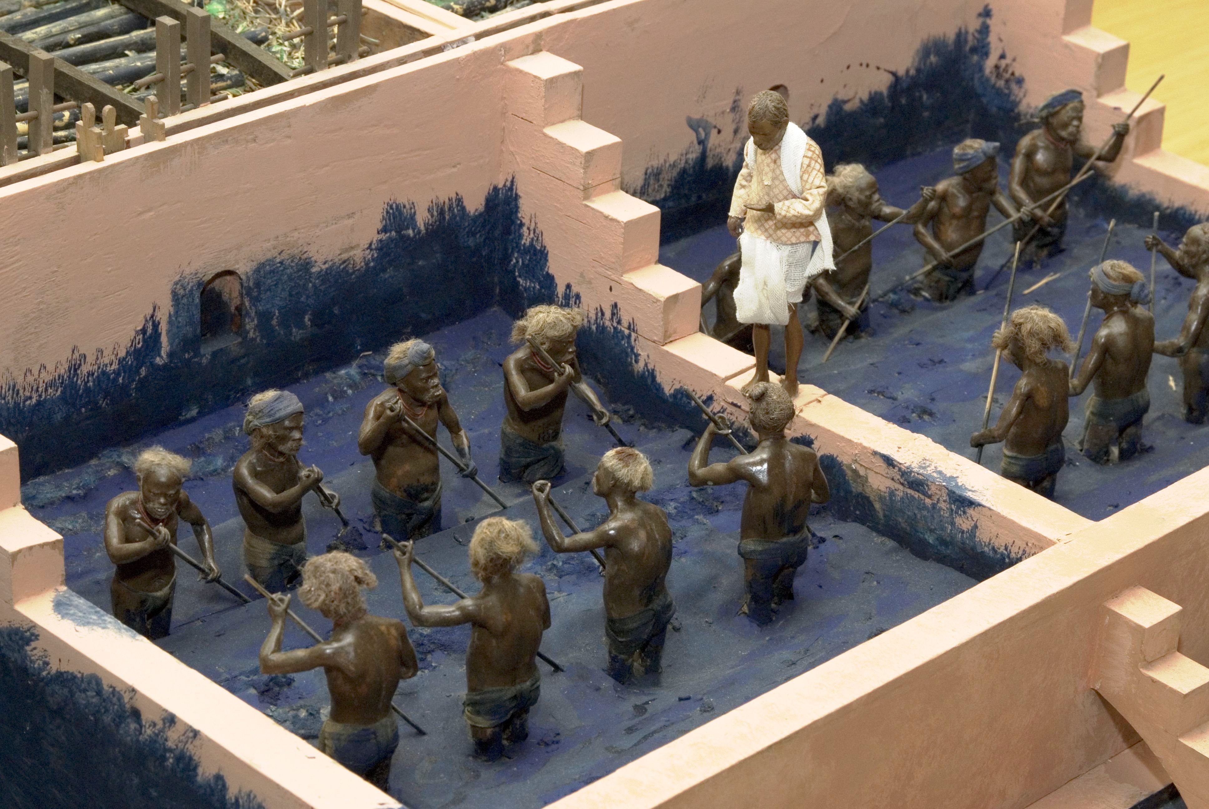 Figurines of workers waist-deep in blue dye, beating the dye with paddles.