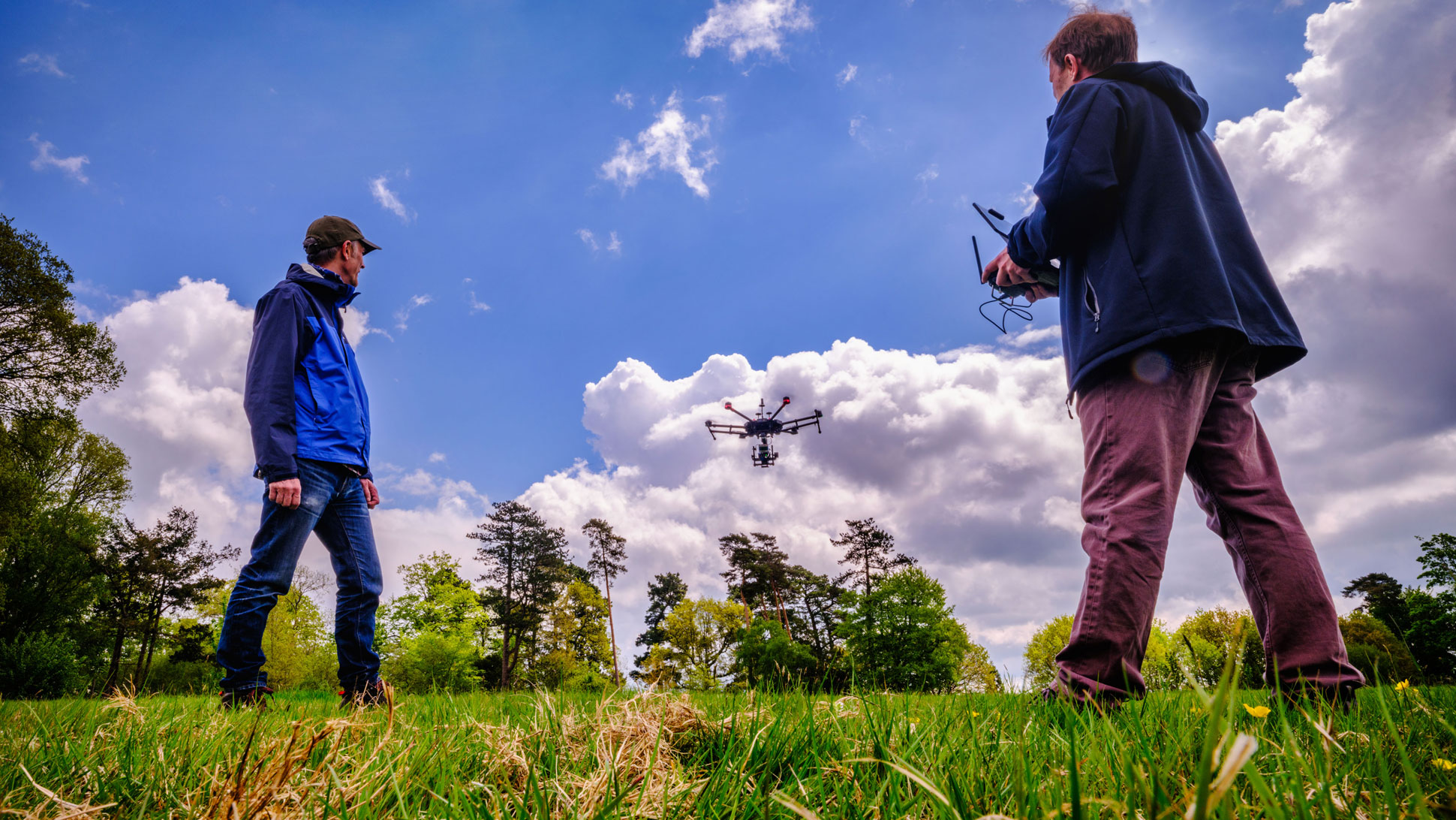Blue sky above two people in a field watching a drone go up
