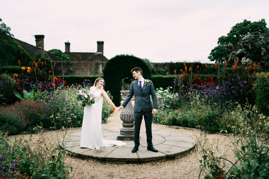 A bride in a white dress and a groom in a blue suit in a Wakehurst garden
