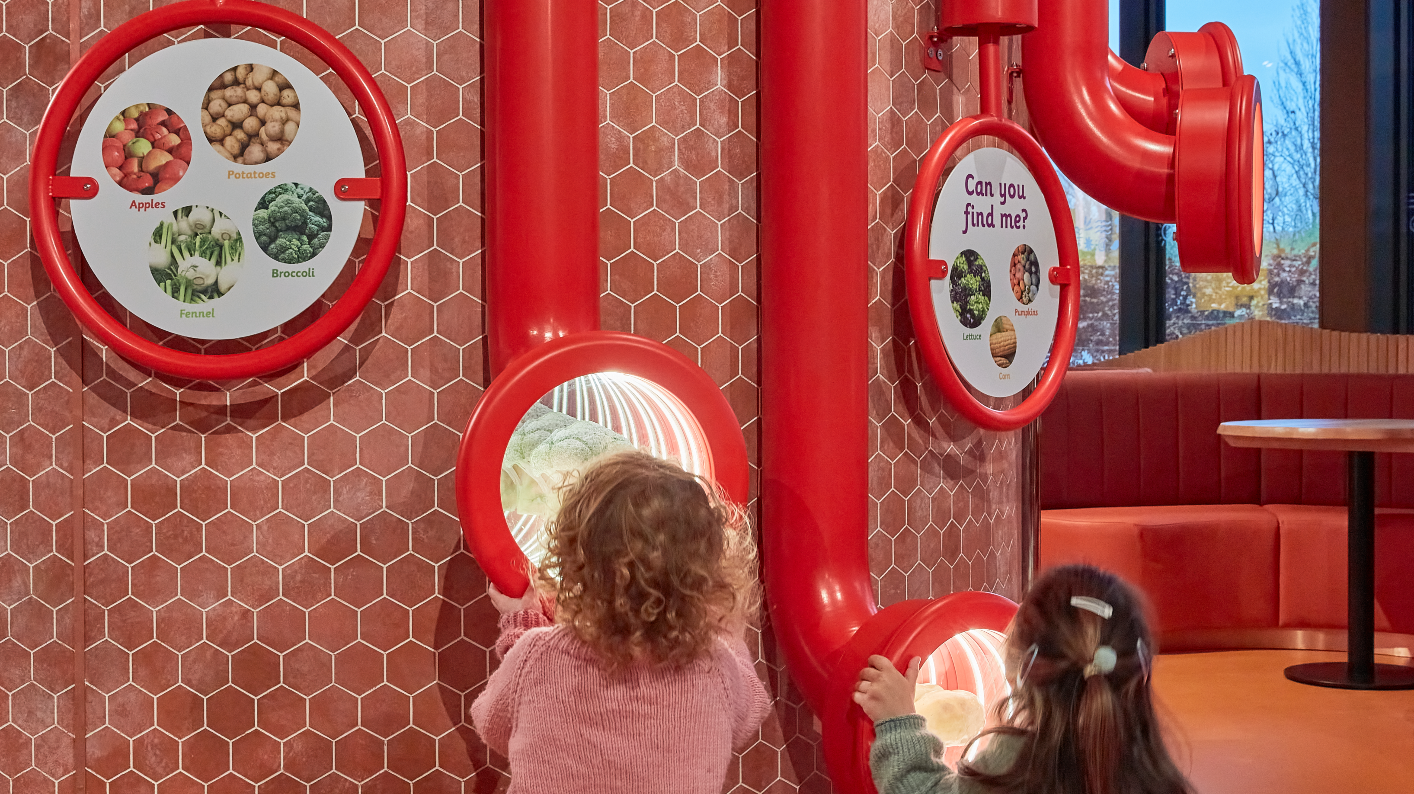 Two children looking through red plastic periscopes at plant foods