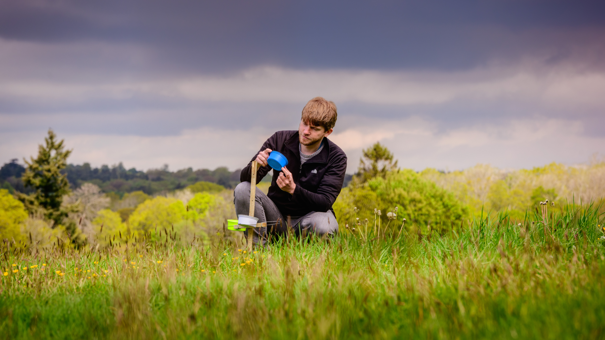 A scientists examines a blue pot whilst crouched in a green field