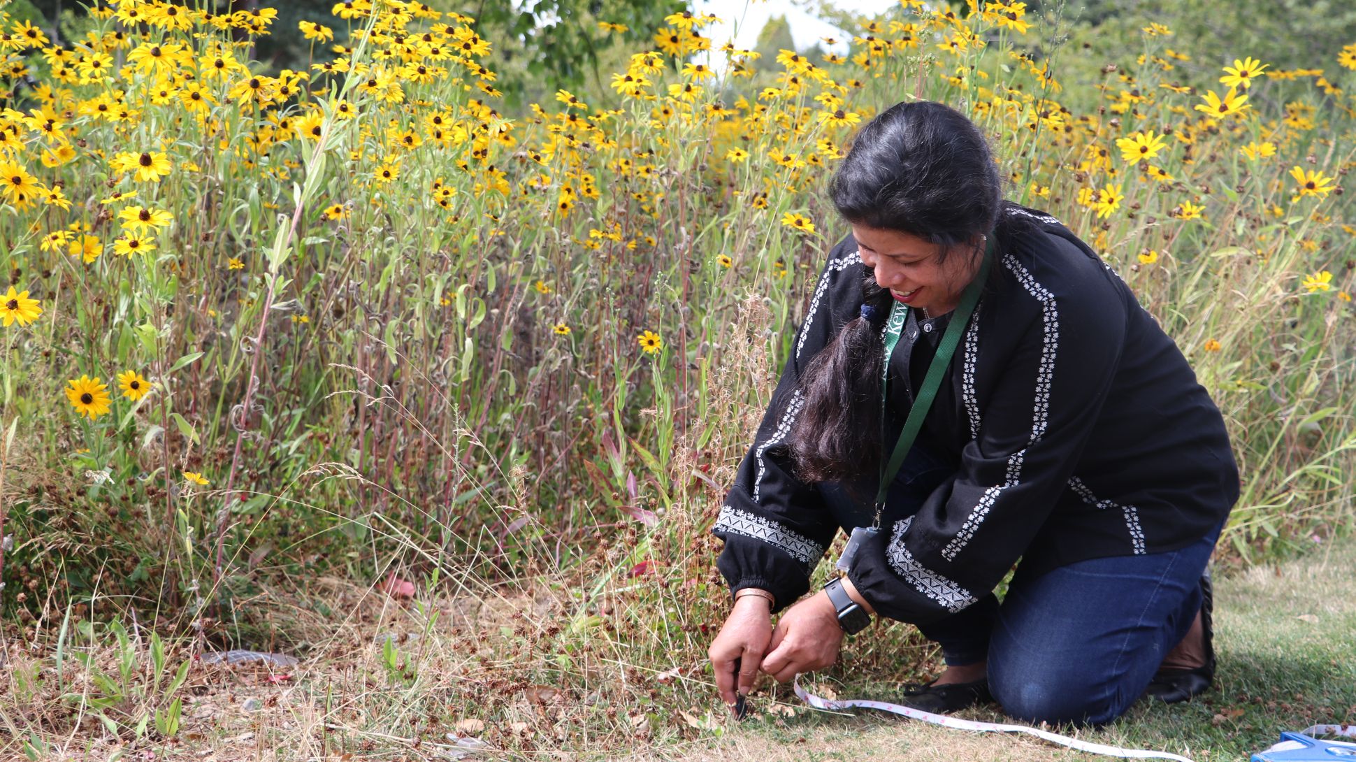A woman uses a measuring tape on the floor next to tall wildflowers