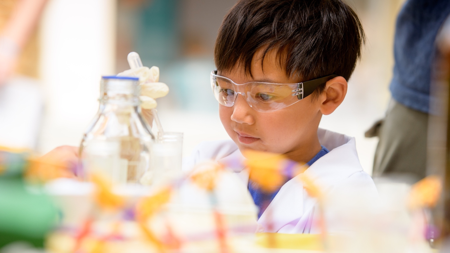 A child takes part in activities wearing a lab coat and goggles