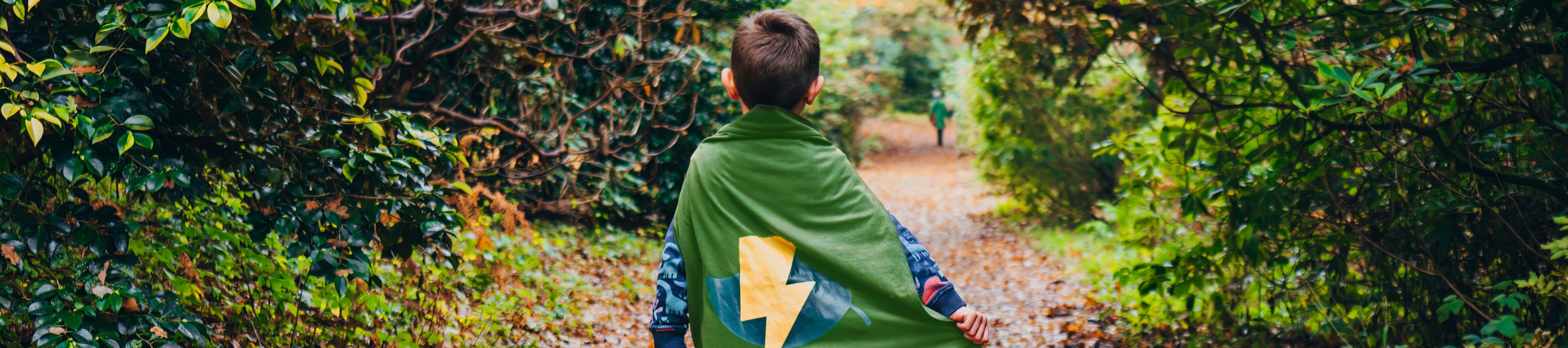 A child walks along a wooded path at Wakehurst wearing a superhero cap with a lightning bolt on it