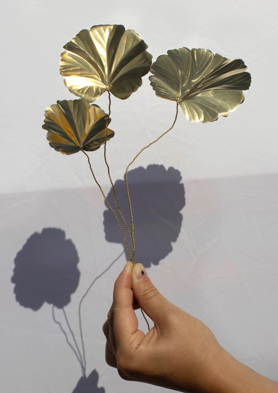 A hand holding a golden metal sculpture of leaves