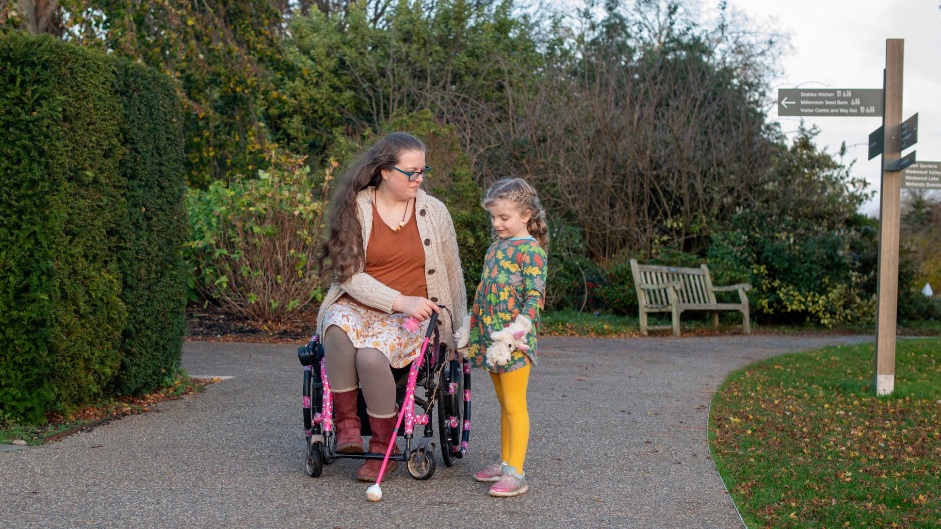 A child with a guide cane stands next to a lady in a wheelchair