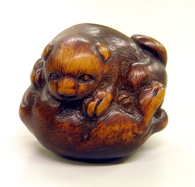 A tiny wooden carving of a dog lying down. It is incredibly detailed for something only a couple of centimetres in size