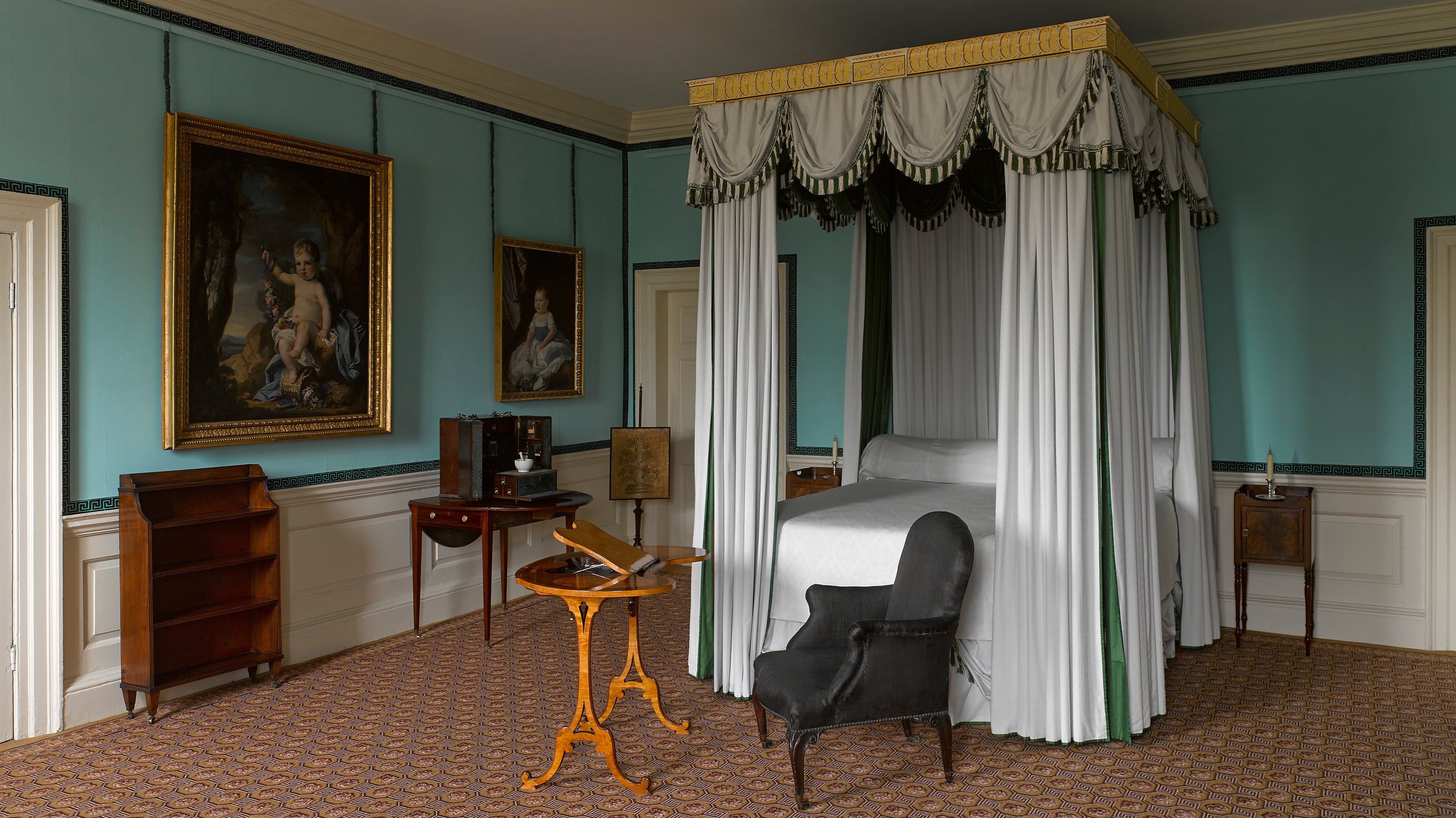 Antique bedroom featuring a curtained bed, gold-framed paintings and a black horsehair armchair in the foreground
