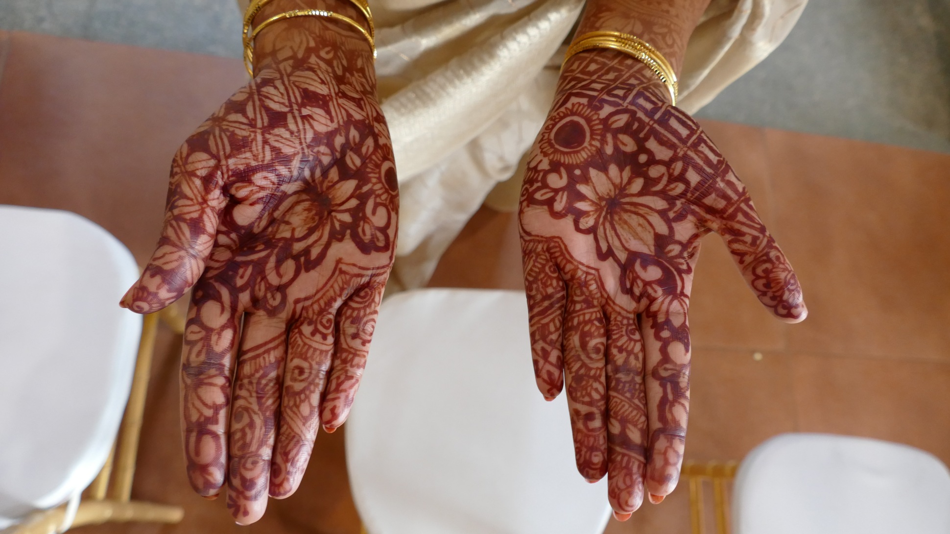 A pair of hands, palms upturned, covered in intricate floral patterns in dark orange 