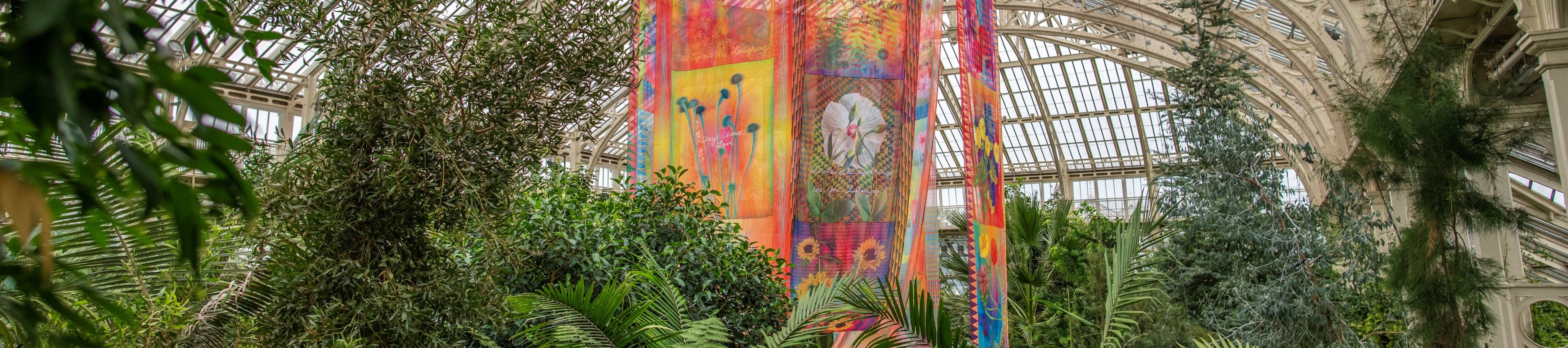 A large colourful hanging banner in a Victorian greenhouse full of green plants