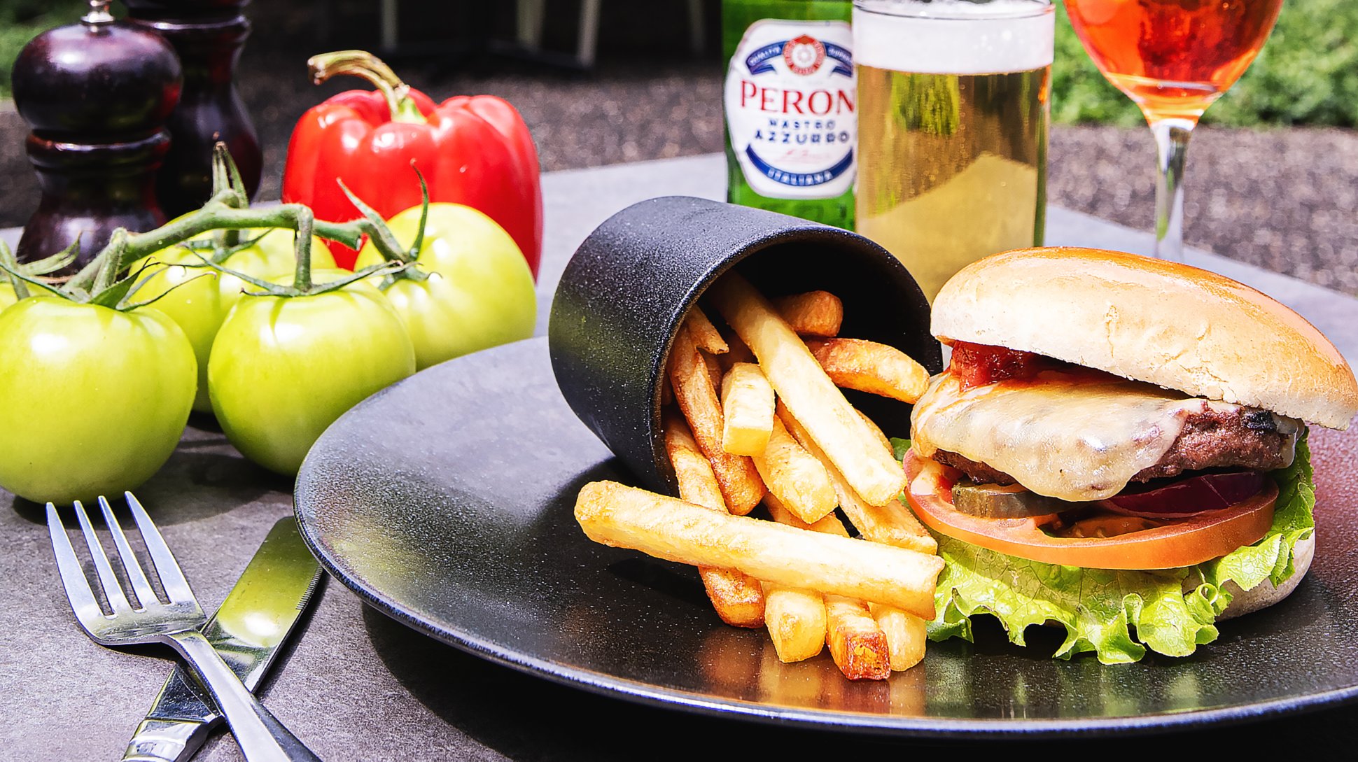 A burger and chips on a plate with large tomatoes in the background
