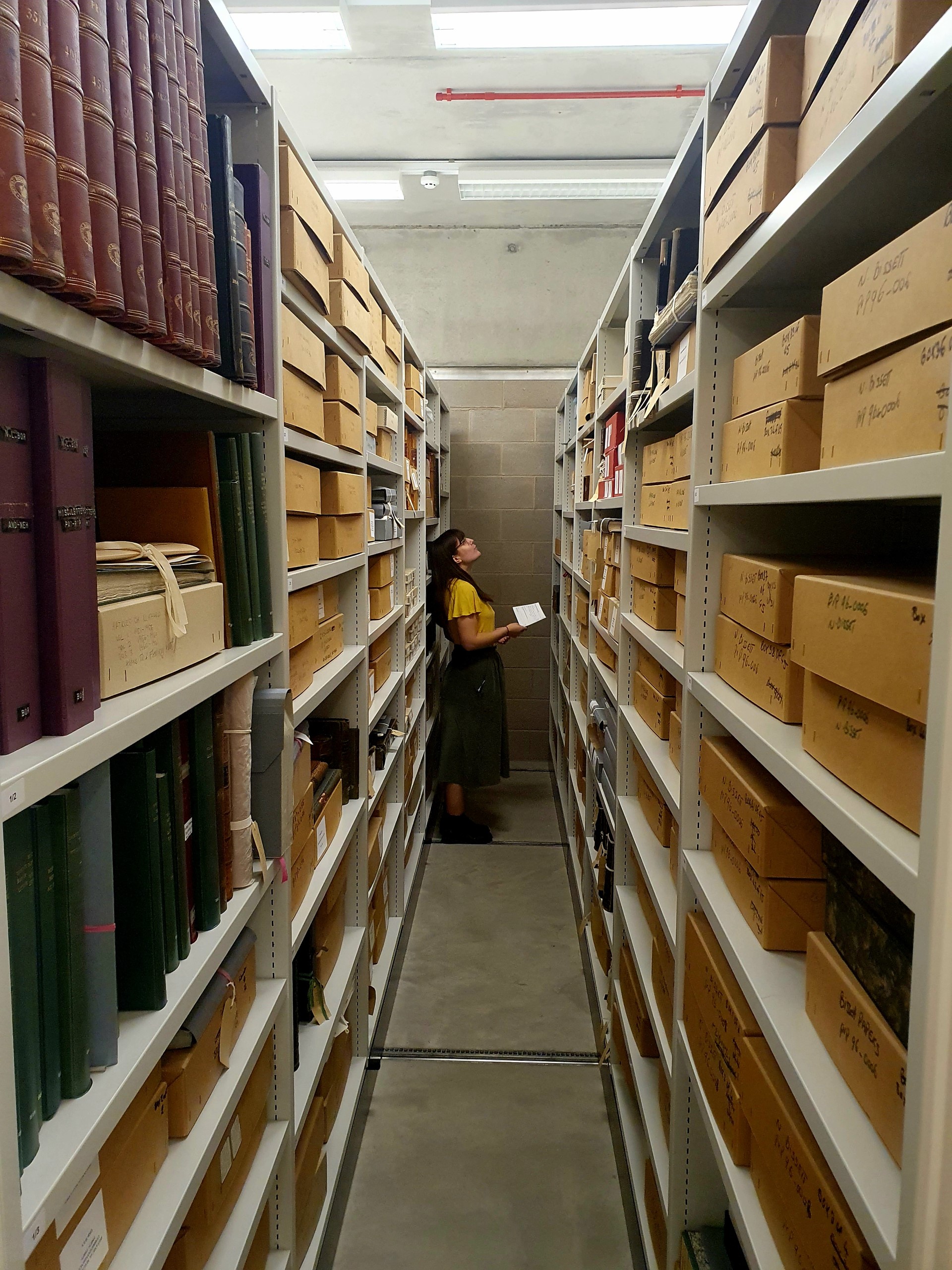 Down a long corridor of full shelves containing books and records, a researcher looks to the resources.