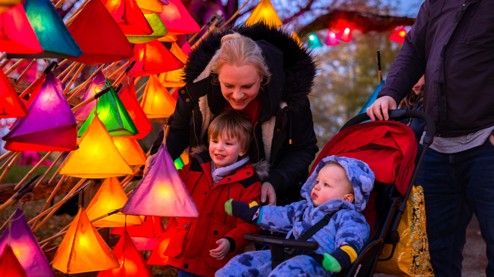 A mother and two young children in front of a row of colourful glowing lanterns.