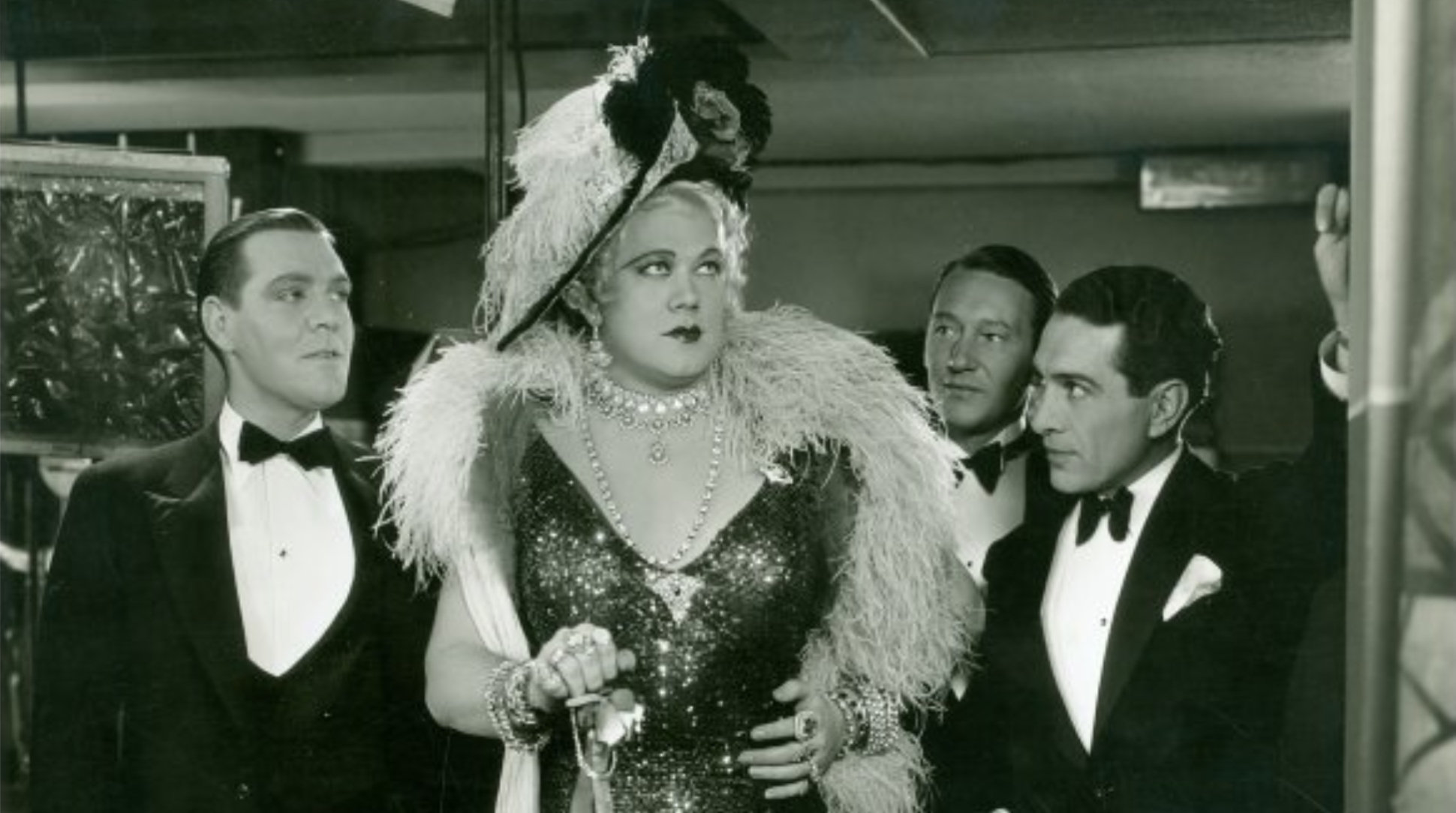 A group of people in suits standing around drag queen Jean Malin