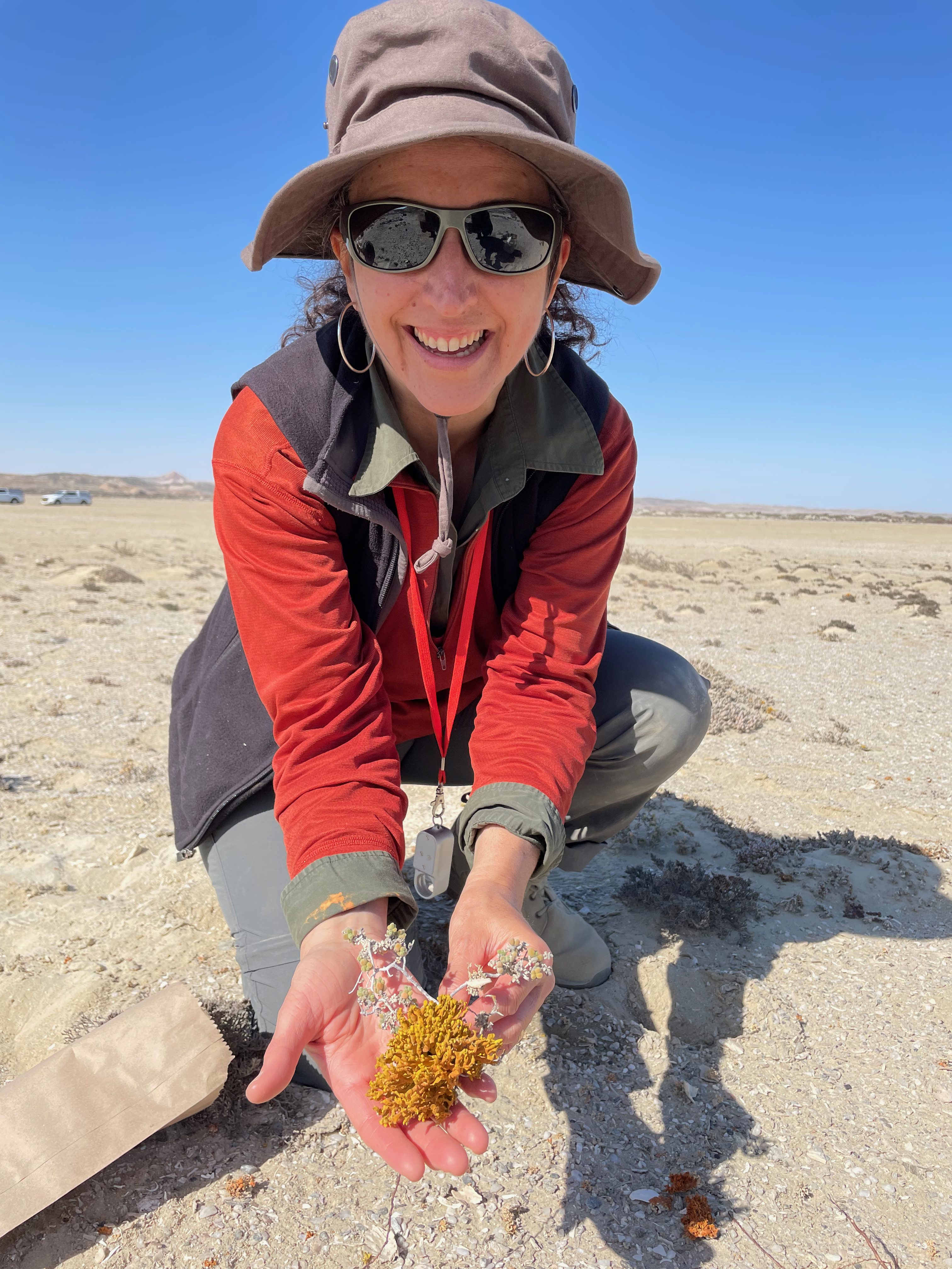 a researcher holds a small orange lichen in her hands among a dry flat landscape