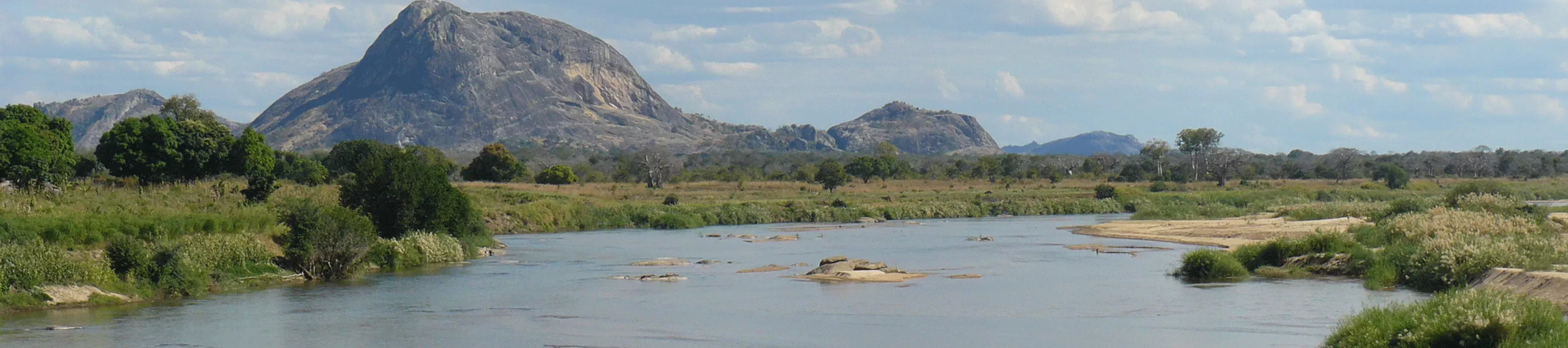 Large rock (Inselberg) in the distance with grassland and river in the foreground