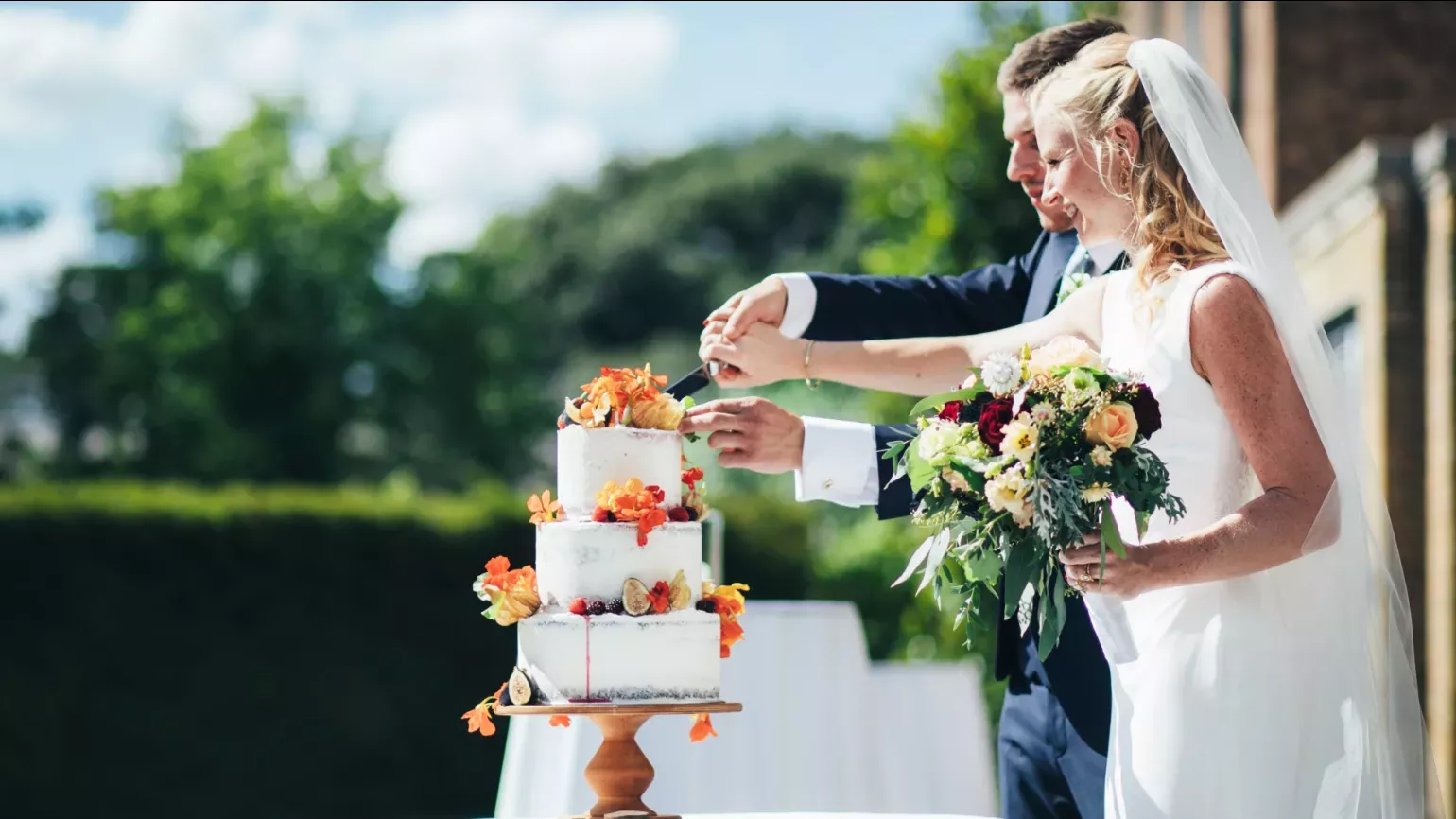 A couple cut into a wedding cake outside