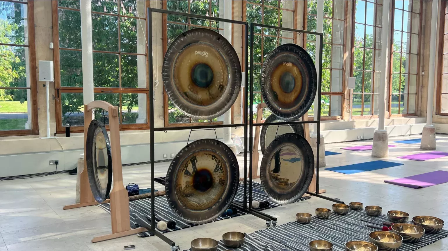 four metal gongs set up in a sunny conservatory, surrounded by yoga mats