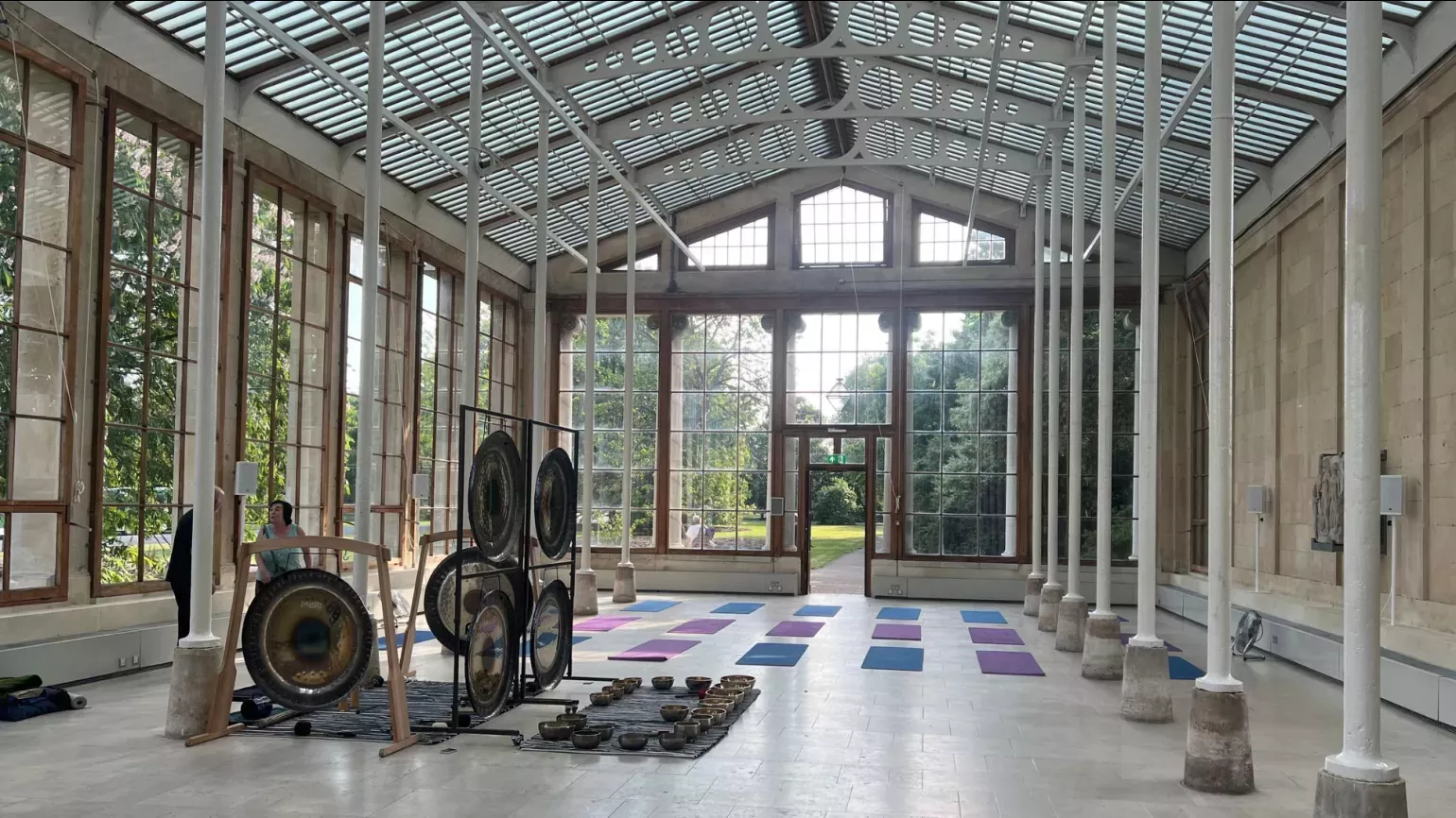 Wide shot of gongs and yoga mats in a sunny conservatory