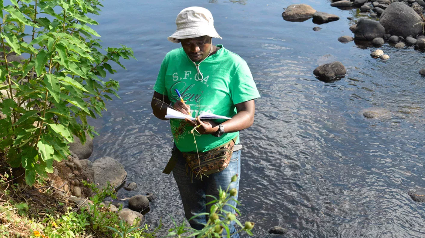 MSc student Kennedy standing in a river with a notebook