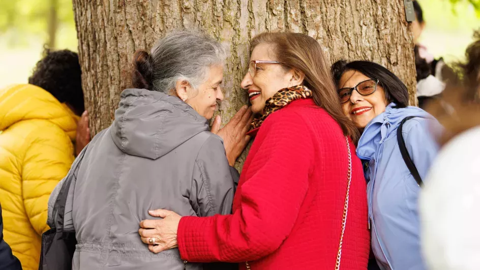 Three women hugging a tree and smiling