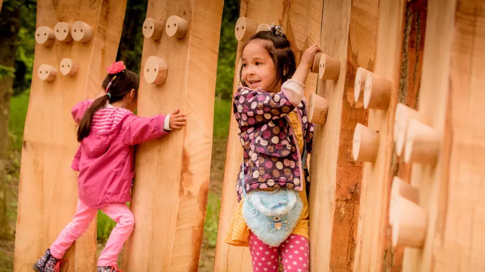 Two girls climb across a wooden activity trail.