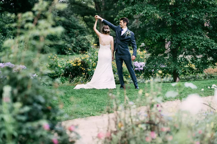A bride in a white dress and a groom in a blue suit dance in a garden © Tom Cullen Photography