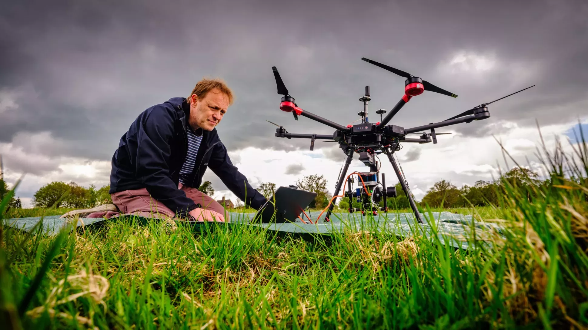 Kew scientist kneeling down in a grassy field with a drone