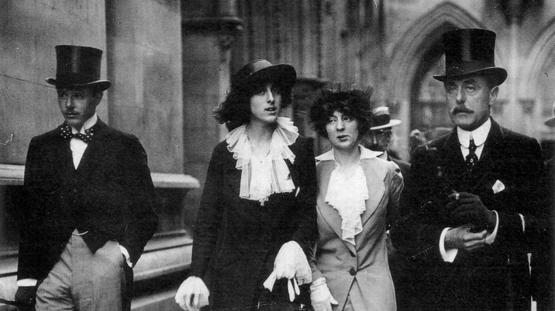 A black and white photo of four people walking down the street, with Vita Sackville West in the middle