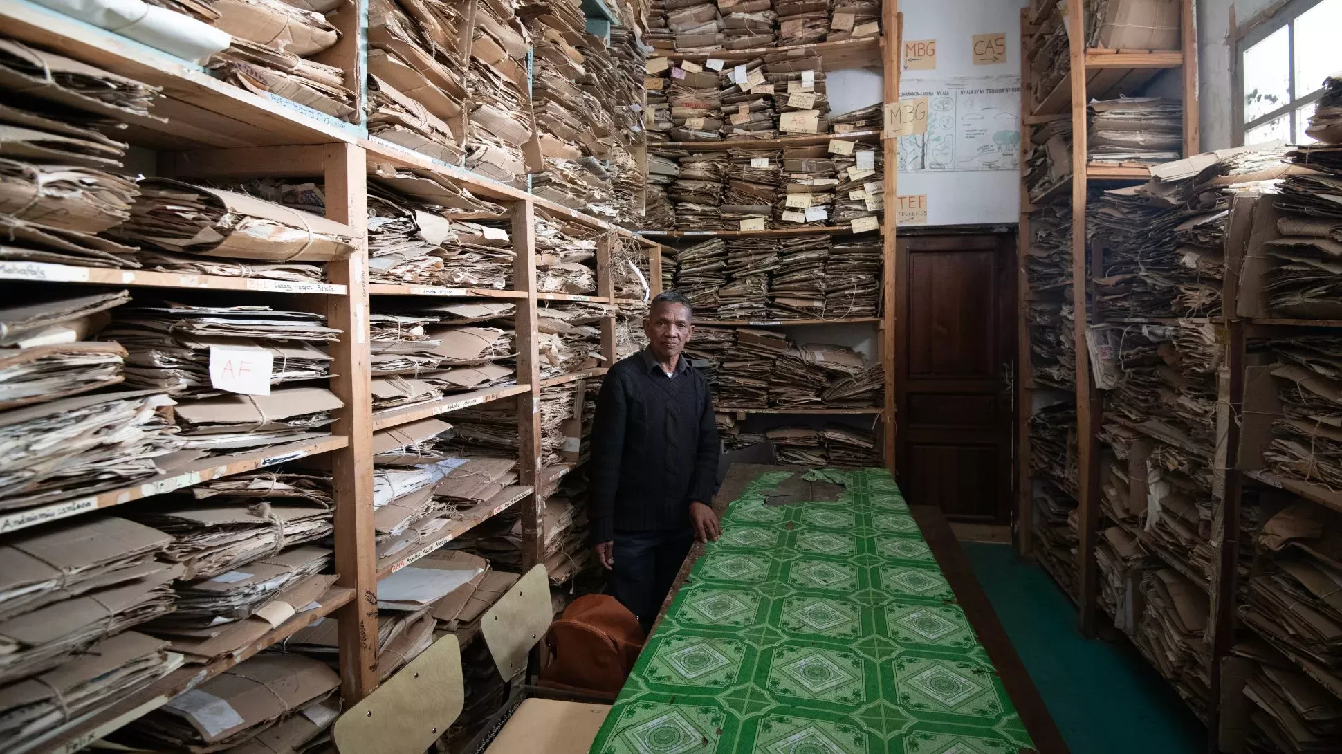 A man standing in a room filled with shelves full of paper