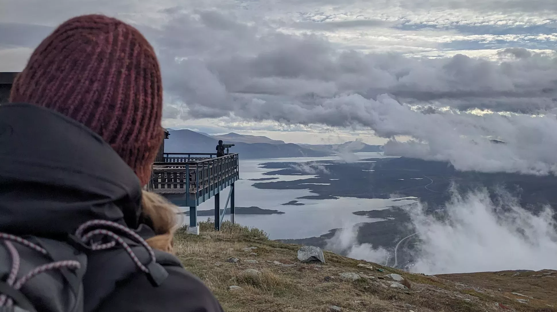 A person in a red woolen hat looking out over a cloudy mountainscape