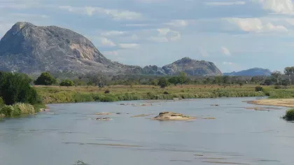 Large rock (Inselberg) in the distance with grassland and river in the foreground